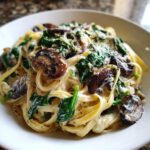 Close-up of creamy mushroom pasta featuring fettuccine, sautéed mushrooms, spinach, and grated Parmesan cheese.