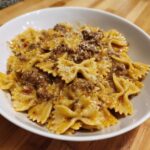 Close-up of creamy parmesan garlic beef bowtie pasta tossed in a rich sauce and topped with grated cheese.