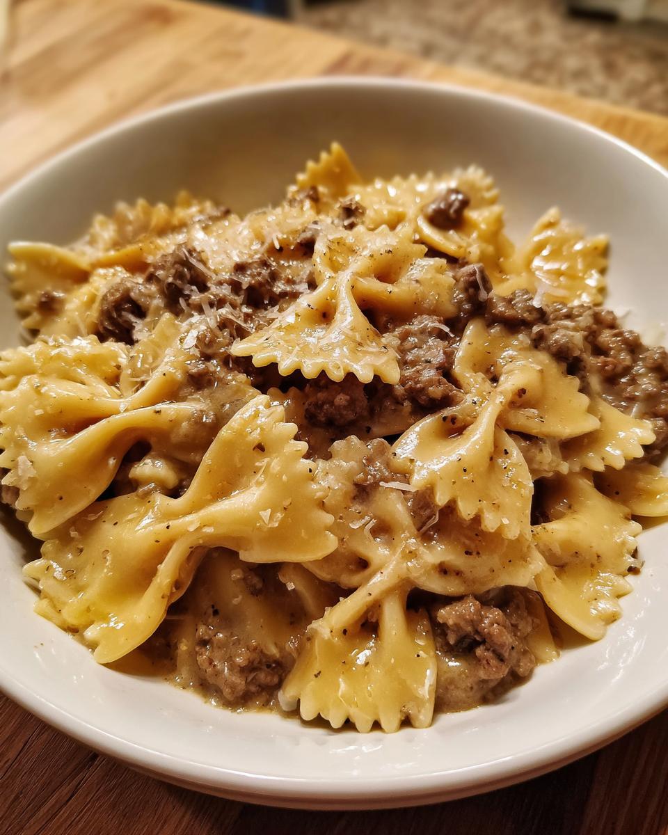 Close-up of creamy parmesan garlic beef bowtie pasta served in a white bowl, topped with grated cheese.