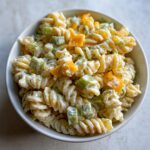 A close-up overhead shot of a creamy pickle pasta salad featuring rotini pasta, diced celery, and orange pickle pieces.
