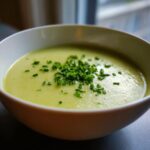 A close-up of creamy potato leek soup topped with freshly chopped green chives in a white bowl.