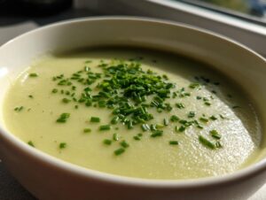 A close-up of creamy potato leek soup in a white bowl, garnished generously with chopped fresh chives.