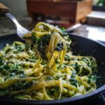 A fork lifting creamy spinach pasta noodles coated in sauce and topped with grated cheese.