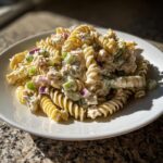 A serving of creamy Tuna pasta salad made with rotini, celery, and red onion on a white plate.