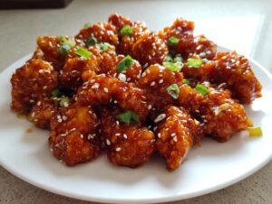 Close-up of crispy, glazed pieces of orange chicken recipe garnished with sesame seeds and chopped green onions.
