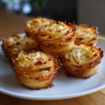 A close-up of several golden-brown, crispy potato stacks baked in a muffin tin, served on a white plate.