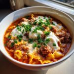 A close-up of a hearty bowl of crockpot lasagna soup topped with dollops of ricotta, meat sauce, and fresh parsley.