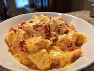 Close-up of creamy crockpot marry me chicken pieces topped with sun-dried tomatoes and grated Parmesan cheese in a white bowl.