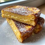 Three slices of golden brown, stuffed french toast piled on a white plate and dusted heavily with powdered sugar.