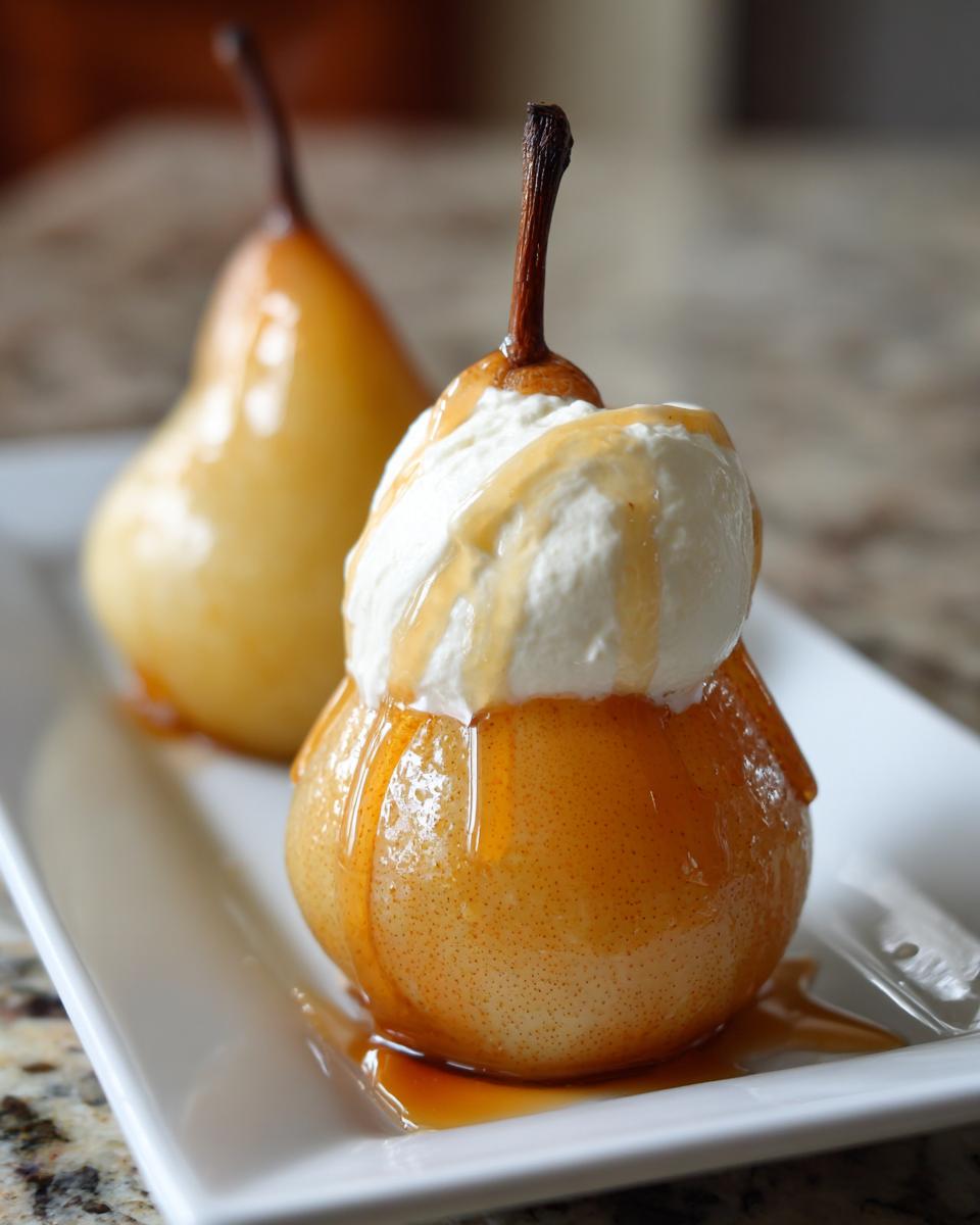 Close-up of a glistening poached pear topped with whipped cream and drizzled with syrup, with another poached pear in the background.