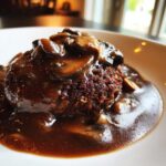 A close-up shot of a perfectly cooked salisbury steak smothered in rich brown mushroom gravy.