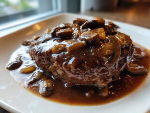 A close-up, mouthwatering photo of an easy salisbury steak patty smothered in rich brown mushroom gravy.