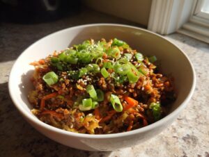 A close-up of a bowl filled with savory egg roll in a bowl mixture, topped with green onions and sesame seeds.