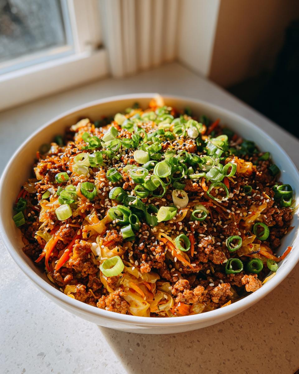 A close-up of a white bowl filled with savory egg roll in a bowl mixture, heavily garnished with sliced green onions and sesame seeds.