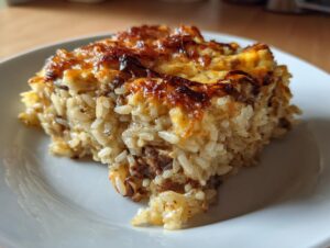 A close-up of a square serving of baked french onion butter rice with a golden, browned cheese topping.