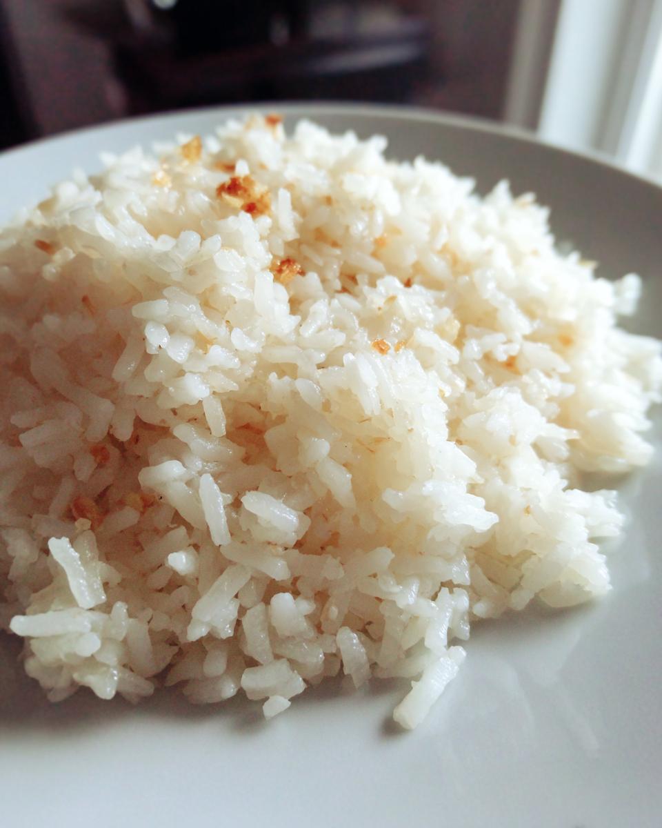 Close-up of fluffy white butter rice served on a light plate, topped with golden toasted bits.