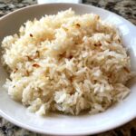 Close-up of a white bowl filled with fluffy, glistening butter rice topped with small, toasted brown bits.