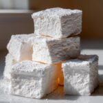 A stack of thick, square homemade marshmallows generously dusted with white powdered sugar.