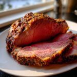 Close-up of a perfectly cooked prime rib recipe roast, showing a dark, seasoned crust and medium-rare pink interior.