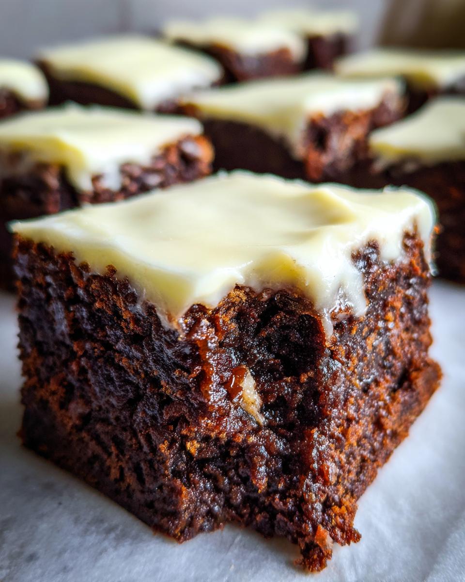 A close-up of a rich, dark gingerbread brownies square topped with thick, creamy white frosting.