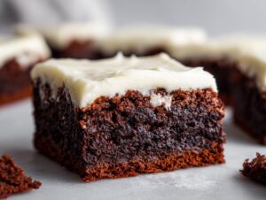 A close-up shot of a rich, dark gingerbread brownies square topped with thick, creamy white frosting.