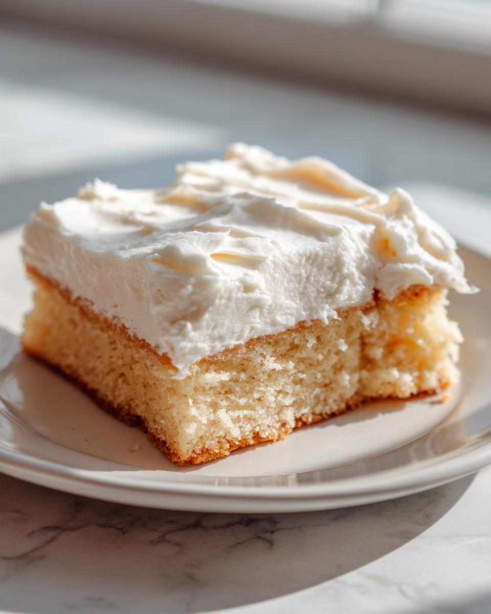 A single serving of a thick, frosted square, resembling sugar cookie bars, sitting on a white plate.