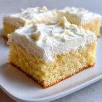A close-up of a square slice of soft, yellow sugar cookie bars topped with thick white frosting.