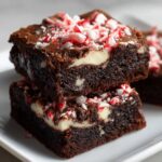 Two fudgy candy cane brownies stacked, showing white chocolate swirls and crushed peppermint topping.