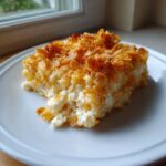 A close-up serving of creamy funeral potatoes recipe with a golden, crunchy cornflake topping on a white plate.