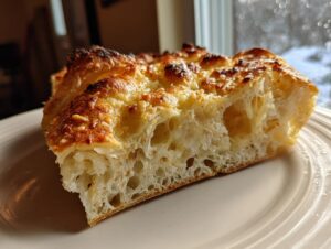 Close-up of a thick slice of Garlic Parmesan bread showing its airy interior and golden, cheesy, slightly charred topping.