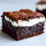 A close-up of a rich, fudgy gingerbread brownies square topped with a thick layer of white frosting.