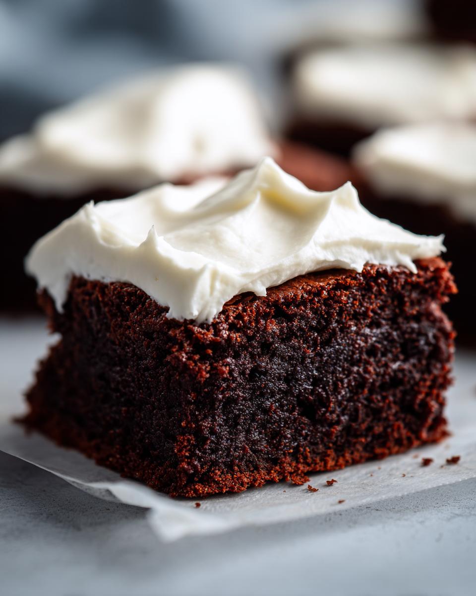 Close-up of a rich, dark slice of gingerbread brownies topped with thick, white cream cheese frosting.