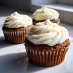 Three rich brown gingerbread cupcakes topped with thick swirls of white cream cheese frosting.