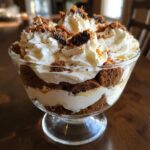 A close-up view of a rich gingerbread trifle layered with cream and topped with whipped cream and crumbs.