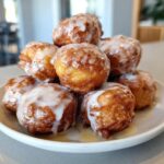 A stack of golden brown baked apple fritters generously drizzled with white glaze.