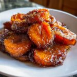 A close-up of thick-cut, deeply caramelized candied sweet potatoes piled high on a white plate.