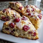 Close-up of a fluffy, triangular cranberry scones topped with a sweet white glaze.