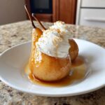 Two beautifully glazed poached pears topped with swirls of whipped cream and a sprinkle of nuts or zest.