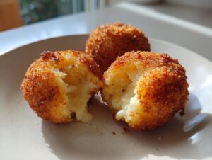 Close-up of three golden-brown, crispy fried rice balls, one broken open revealing a melted, cheesy interior.