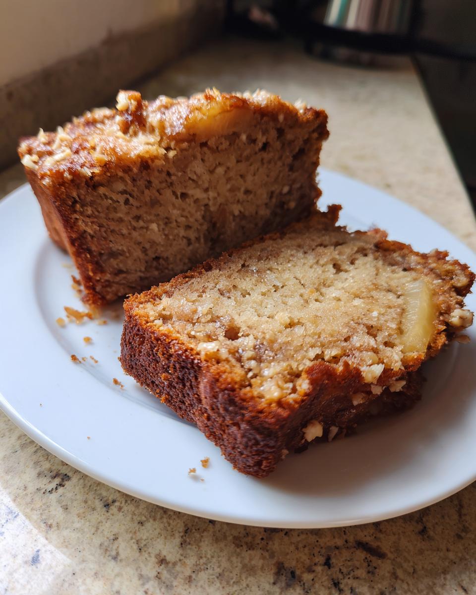 Two thick slices of moist Hawaiian banana bread with a caramelized, nutty topping on a white plate.