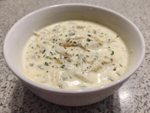 A white bowl filled with rich, creamy homemade cream of chicken soup, topped with herbs.