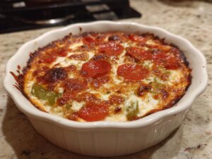A close-up of a bubbling, baked pepperoni pizza dip topped with melted cheese and green peppers in a white ramekin.