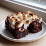 A rich, fudgy square of hot chocolate brownies topped with toasted marshmallows served on a white plate.