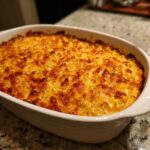 A baked, bubbling mexican street corn dip in a white oval casserole dish with a golden brown, cheesy top.