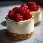 Close-up of a single-serving Protein Cheesecake in a glass jar, topped with bright red fresh raspberries.
