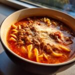 Close-up of a rich, red bowl of Instant Pot Lasagna Soup topped with ground meat and melted Parmesan cheese.