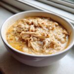 Close-up of a white bowl filled with creamy Instant Pot White Chicken Chili, showing shredded chicken and white beans.