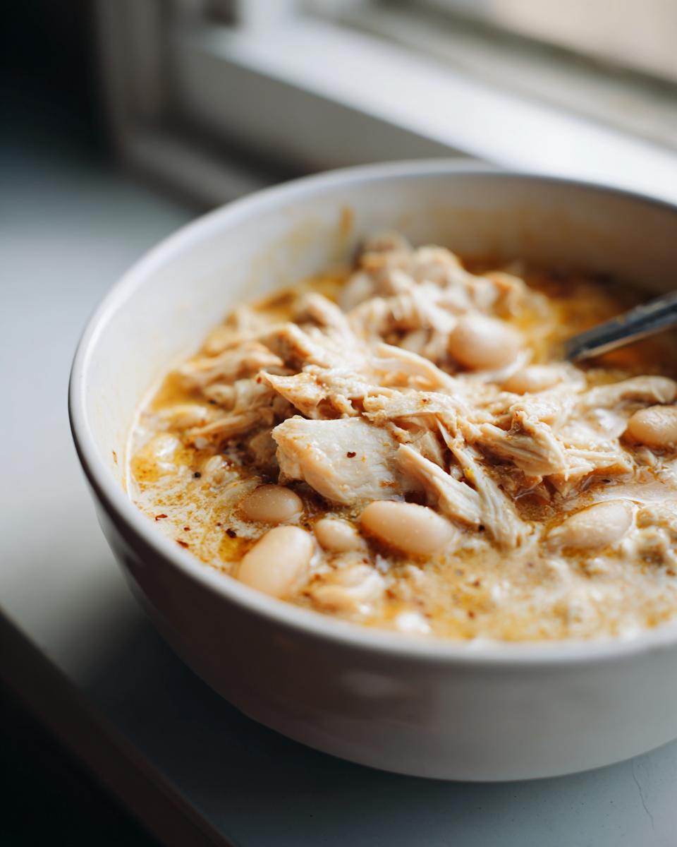 Close-up of a white bowl filled with creamy instant pot white chicken chili, featuring shredded chicken and white beans.