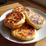 Four freshly cooked, golden brown Irish potato farls stacked slightly on a white plate.