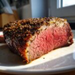 Close-up of a perfectly cooked, medium-rare rib roast slice with a thick, dark pepper crust.